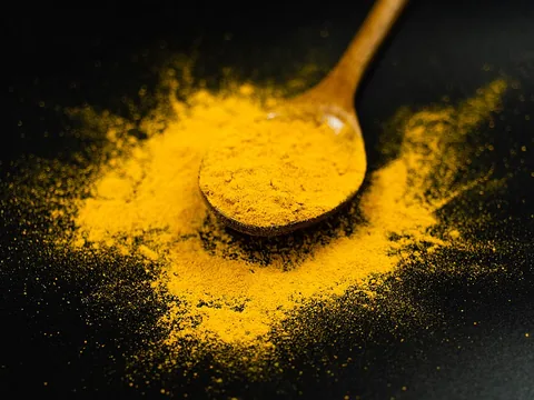 Bright yellow turmeric powder on a wooden spoon